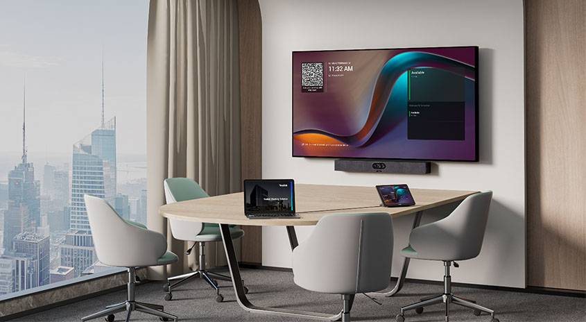 Kleiner Konferenzraum mit Wandmonitor und Yealink MeetingBar A25 darunter; Tisch mit vier Stühlen, Laptops/Tablets und Fenster mit Stadtaussicht.