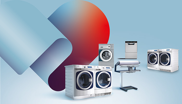 Gruppe von gewerblichen Electrolux-Geräten vor hellblauem Hintergrund mit einer abstrakten blau-rot-violetten Grafikform: mehrere Waschmaschinen und Wäschetrockner mit blauen Bullaugen, eine gewerbliche Spülmaschine sowie ein Bügel-/Mangelgerät auf Ständer. 