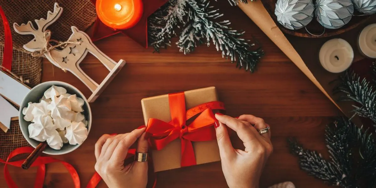 Ein Paket wird mit einer roten Schleife verpackt inmitten von Weihnachtsdeko.