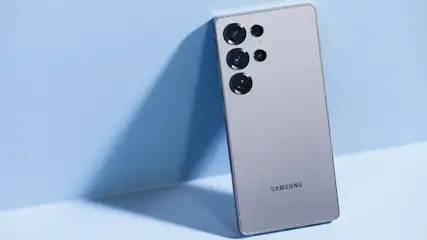 Rückseite eines silbernen Samsung Galaxy S25 Smartphones vor blauem Hintergrund.