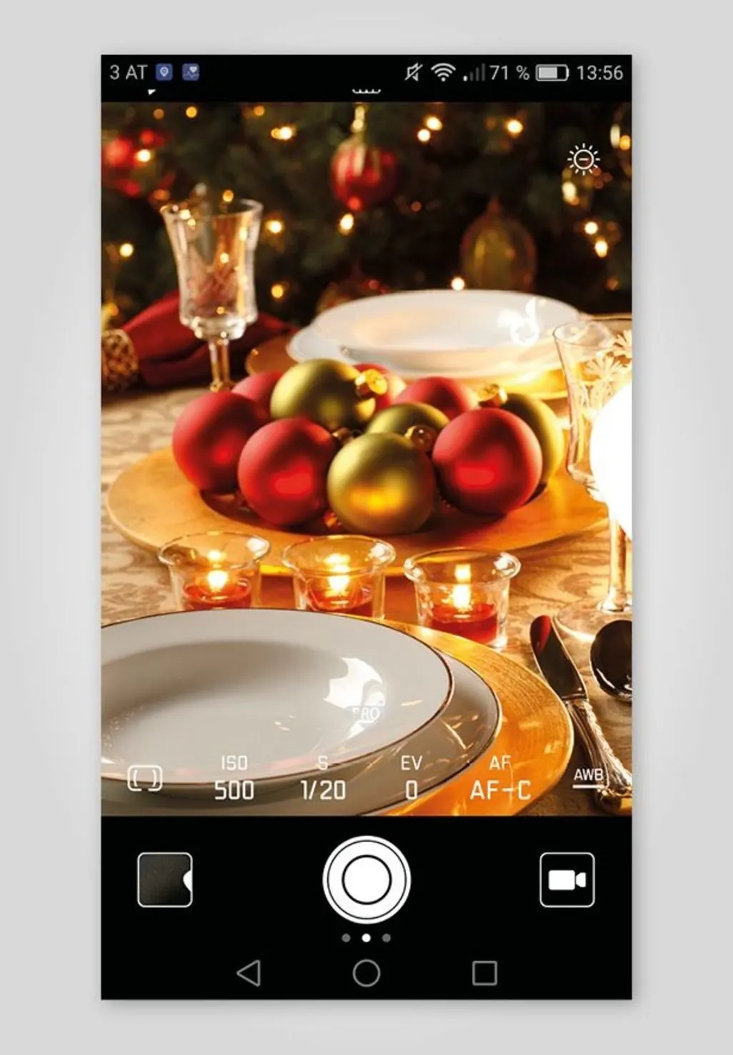 Gedeckter Tisch mit Weihnachtskugeln und Kerzen im Kameradisplay eines Smartphones