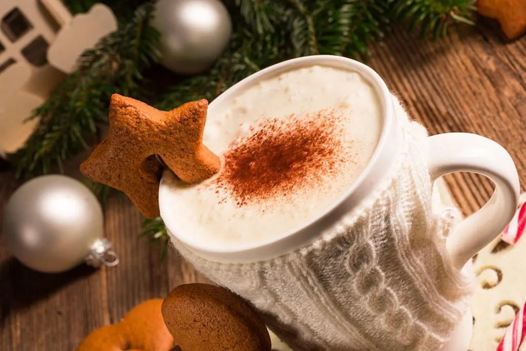 Tasse mit Heißgetränk im Strickpulli und Sternen-Keks vor Weihnachtsdekoration.