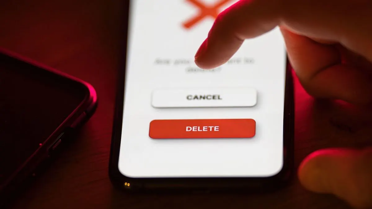 Finger berührt auf einem Smartphone den roten Button mit der Aufschrift DELETE, daneben befindet sich ein weißer Button mit CANCEL.