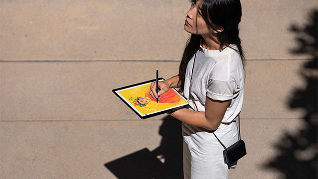 Eine Person in Weiß hält ein digitales Tablet mit einem Stift vor einer beigen Wand.