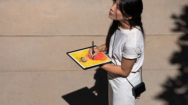 Eine Person in Weiß hält ein digitales Tablet mit einem Stift vor einer beigen Wand.