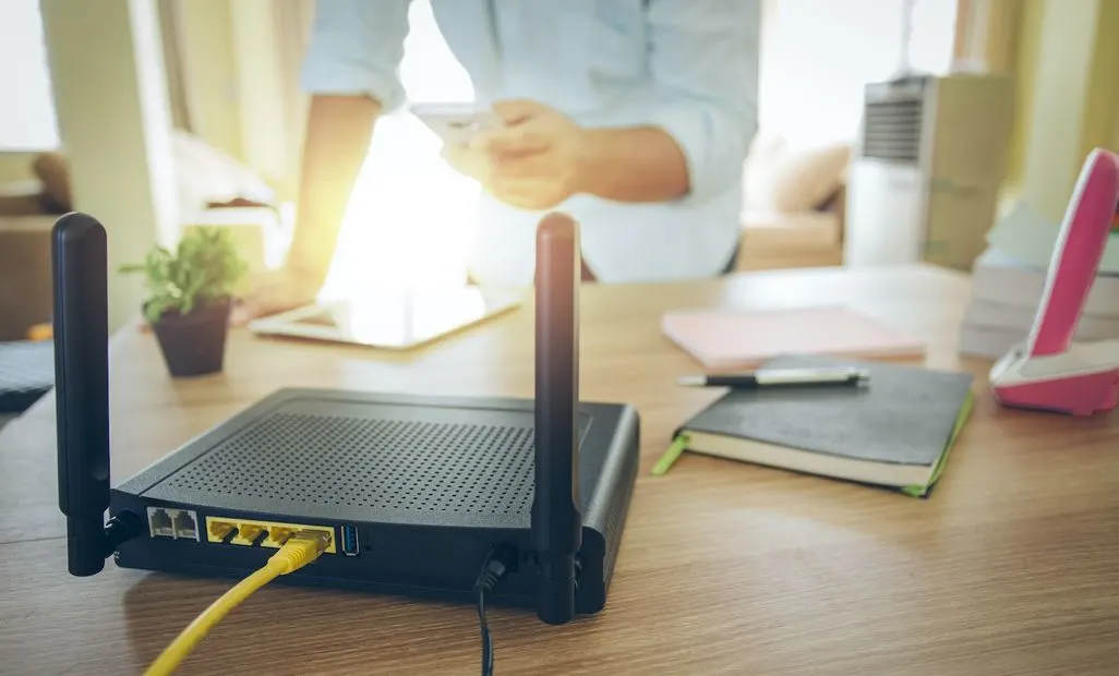 Schwarzer WLAN-Router mit gelben Ethernet-Kabeln steht auf Holztisch.