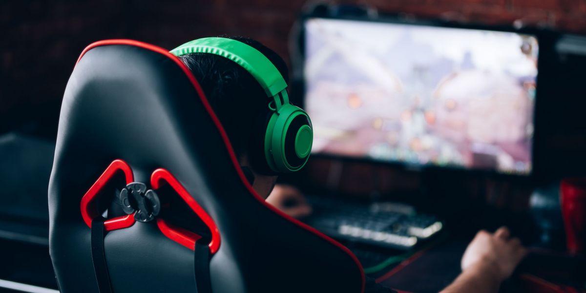 Person mit grünen Kopfhörern sitzt auf einem Gaming-Stuhl vor einem Computerbildschirm und spielt ein Videospiel.