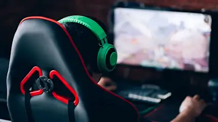 Person mit grünen Kopfhörern sitzt auf einem Gaming-Stuhl vor einem Computerbildschirm und spielt ein Videospiel.