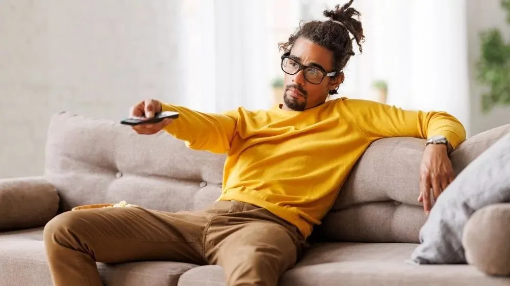 Mann sitzt auf dem Sofa und bedient Fernbedienung