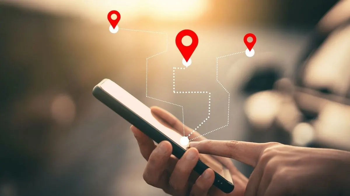 Hand haelt ein Smartphone mit digitalen Standortmarkern und Linien zur Navigation