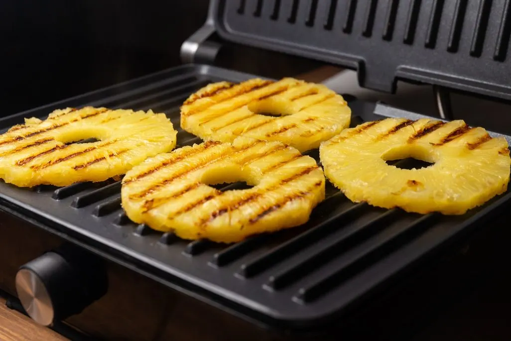 Vier Scheiben Ananas werden auf einem Kontaktgrill mit Grillstreifen gegrillt.