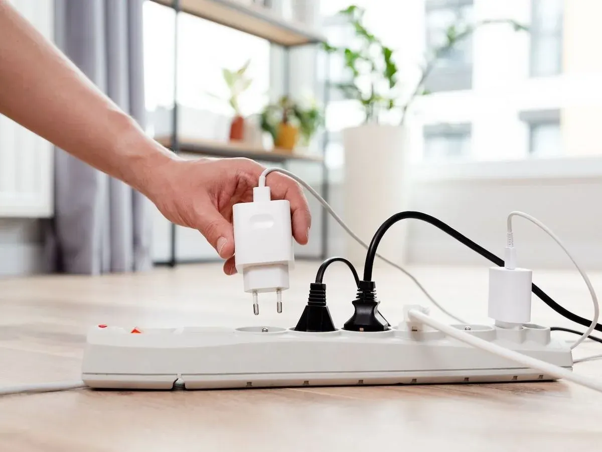 Hand zieht Stecker von einem Stromfresser im Haushalt aus der Steckdosenleiste.