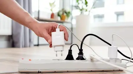 Hand zieht Stecker von einem Stromfresser im Haushalt aus der Steckdosenleiste.