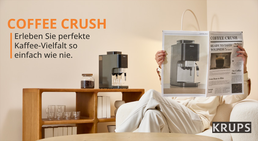 Person hält COFFEE CRUSH Zeitung neben Krups Kaffeemaschine auf Holzregal. Erleben Sie perfekte Kaffee-Vielfalt so einfach wie nie.
