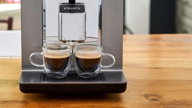 Krups Kaffeemaschine füllt zwei Gläser mit dunklem Kaffee auf einem Holztisch.