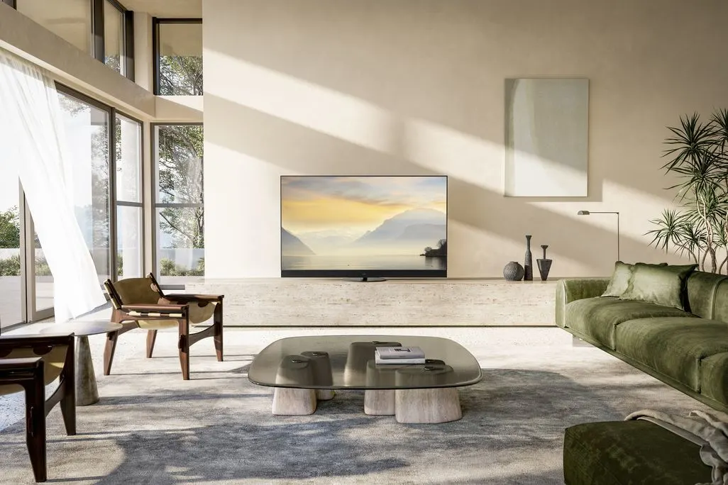 Ein Fernseher mit Landschaftsbild steht in einem hellen modernen Wohnzimmer mit großen Fenstern.
