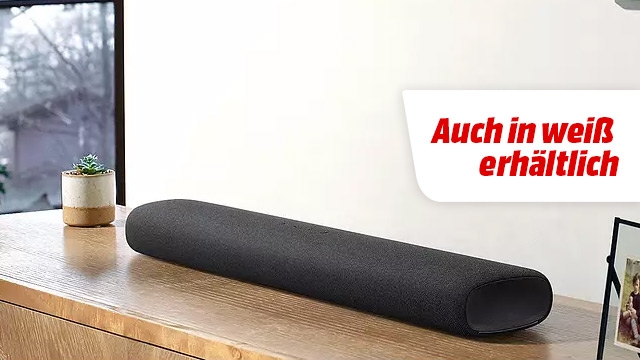 Ein schwarzer Lautsprecher liegt auf einem Holzschrank, daneben eine Pflanze und ein Rahmen. Text: "Auch in weiß erhältlich".