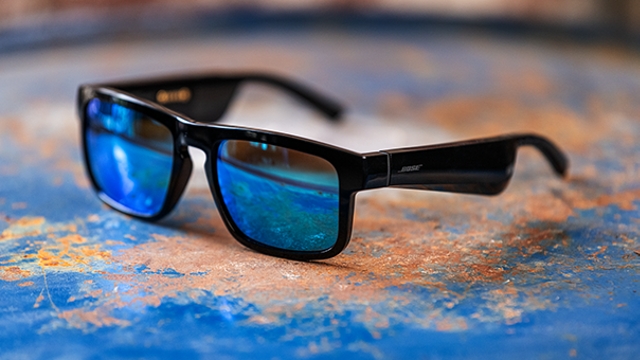 Eine schwarze Sonnenbrille mit blauen Gläsern liegt auf einer blau-braunen Oberfläche.
