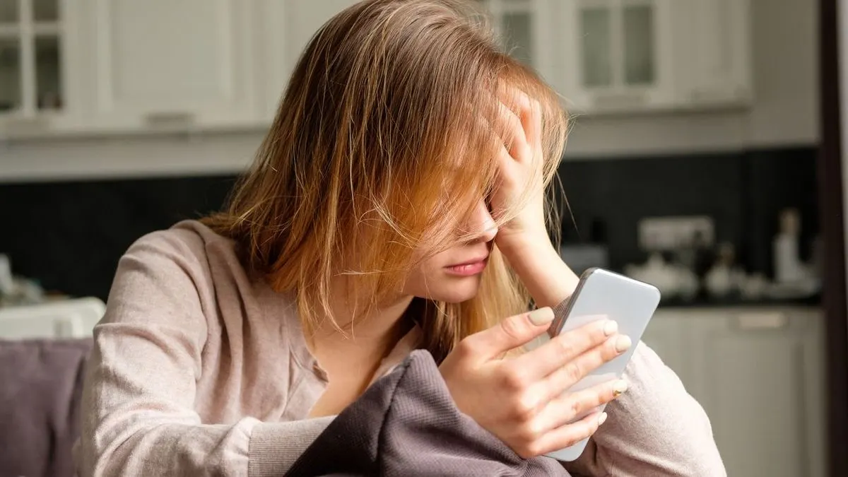 Frau stuetzt ihren Kopf in die Hand und blickt auf ihr Smartphone