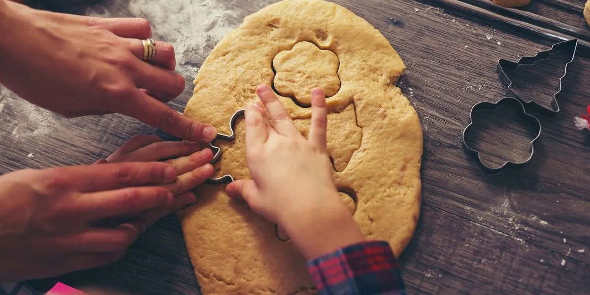 Kinderhände und Erwachsenehände stechen gemeinsam Kekse aus einem Teig.