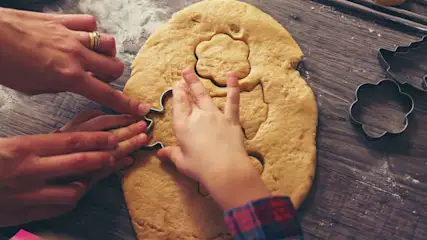 Kinderhände und Erwachsenehände stechen gemeinsam Kekse aus einem Teig.