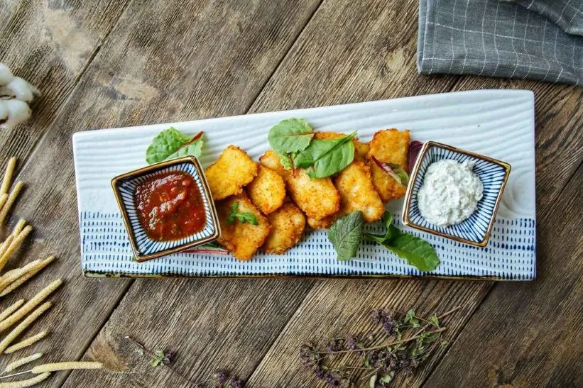 Rechteckiger Teller mit veganen Nuggets, zwei Dips und frischen Kräutern.