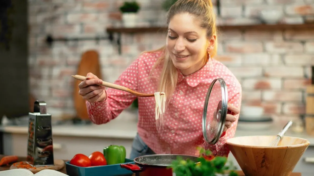 Frau prüft mit einem Holzlöffel Spaghetti in einer Küche.