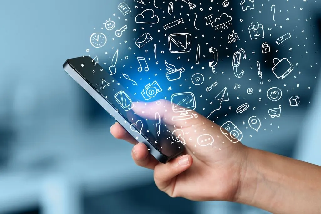 Eine Hand hält ein Smartphone, aus dem viele digitale Symbole und Icons herausfliegen.