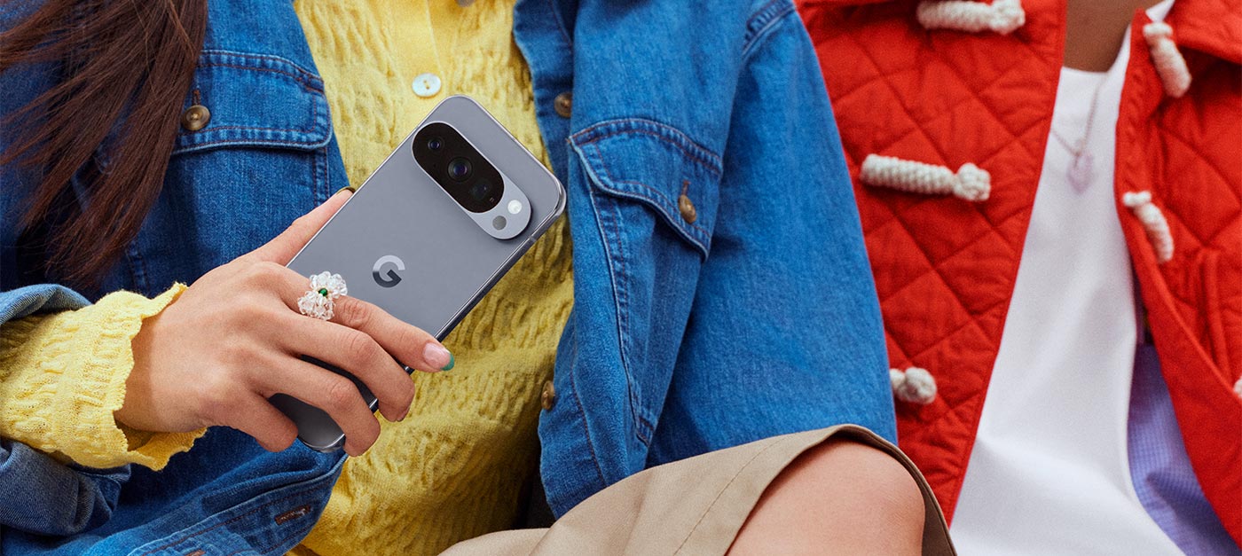  ALT-Text-Vorschlag:  „Person in gelber Strickjacke und Jeansjacke sitzt und hält ein graues Google Smartphone mit breitem Kameramodul in der Hand.“