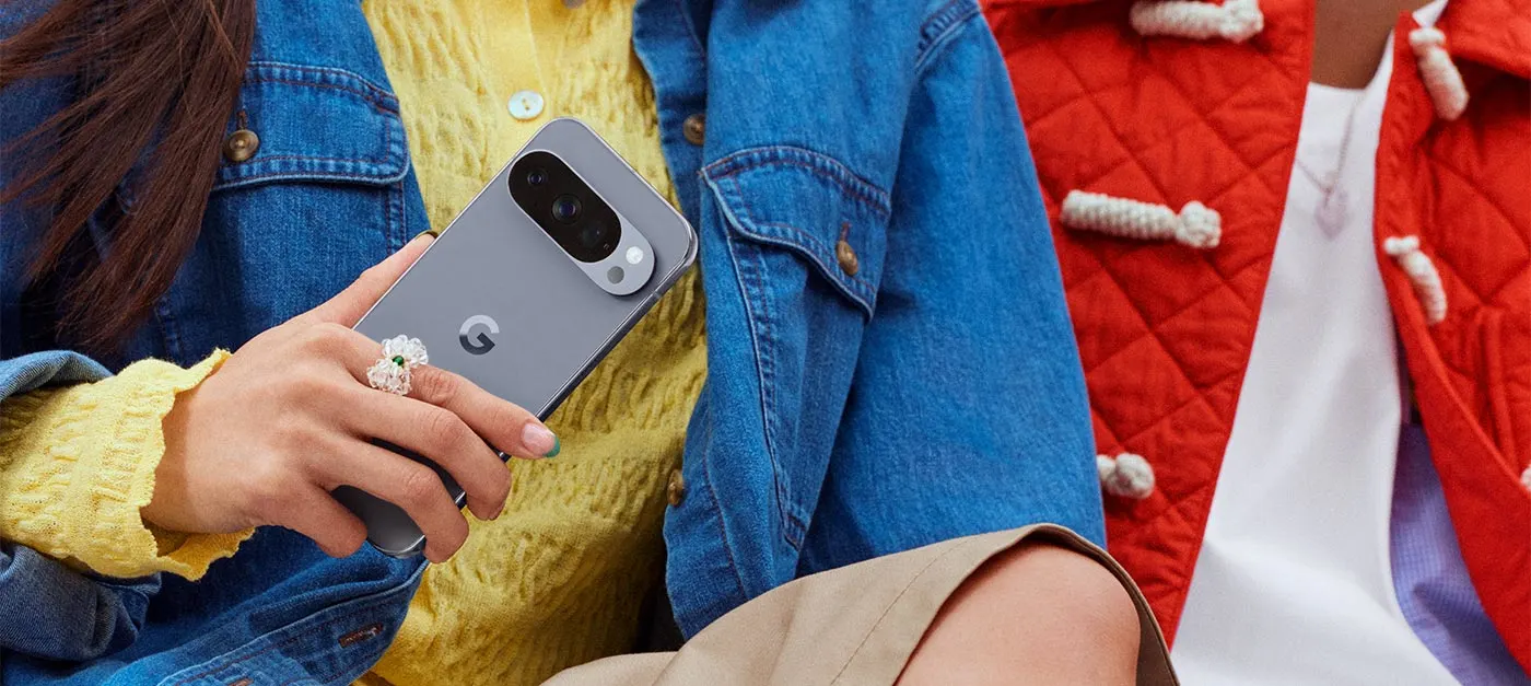 ALT-Text-Vorschlag: „Person in gelber Strickjacke und Jeansjacke sitzt und hält ein graues Google Smartphone mit breitem Kameramodul in der Hand.“