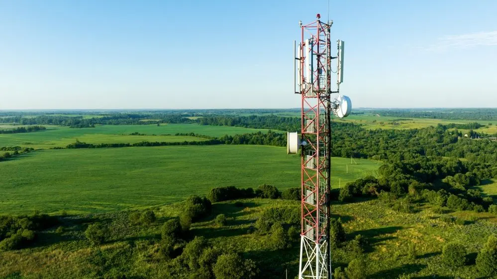 Ein Mobilfunkmast steht auf einer grüne Wiese in einer weiten Landschaft.