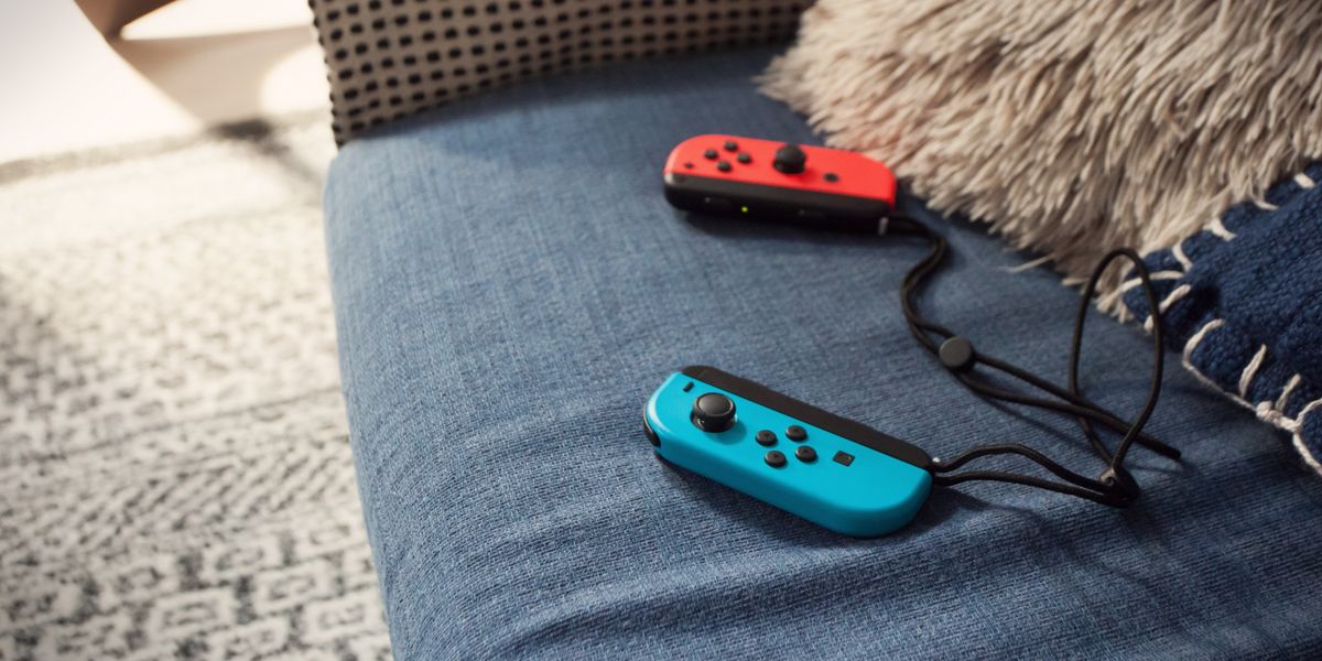 Roter und blauer Nintendo Switch Joy-Con Controller liegen auf einem blauen Sofa neben Kissen