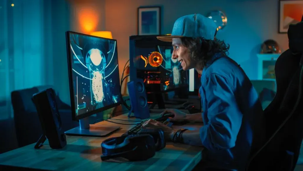 Jugendlicher sitzt lächelnd vor seinem Gaming-Setup und spielt am PC