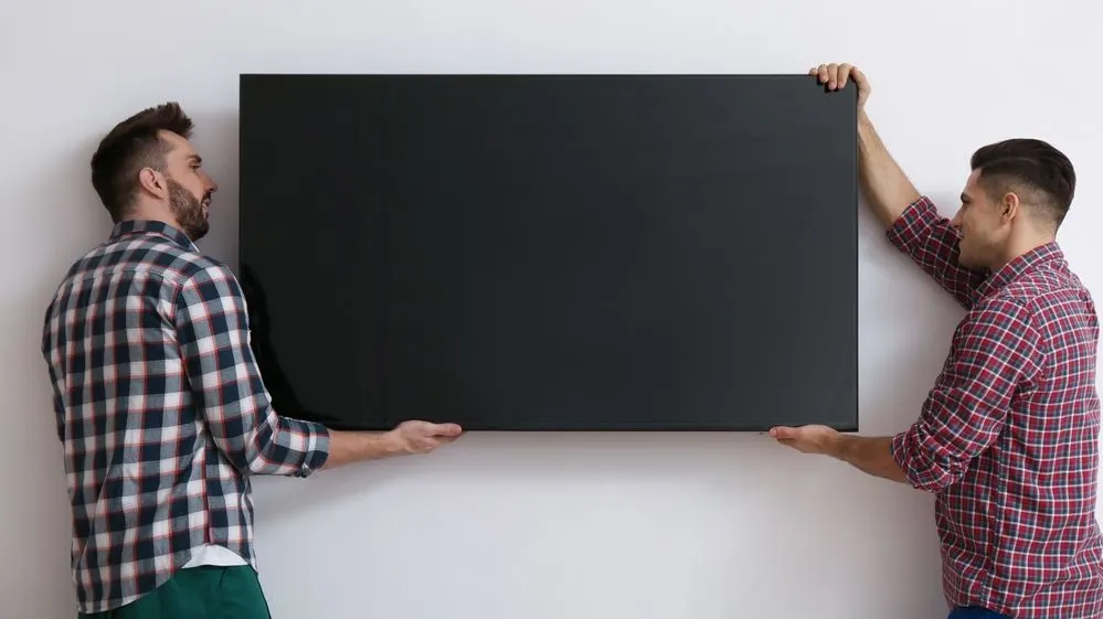 Zwei Personen hängen gemeinsam einen Fernseher an die Wand.