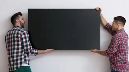 Zwei Personen hängen gemeinsam einen Fernseher an die Wand.