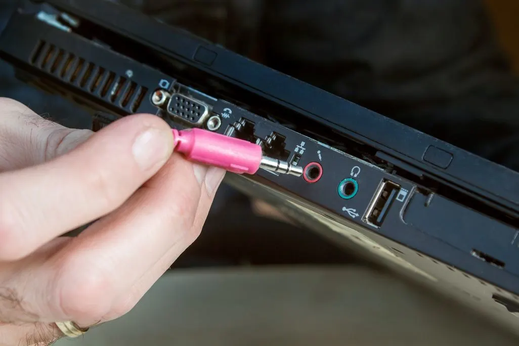 Hand steckt pinken Audiostecker in Laptop-Anschluss.