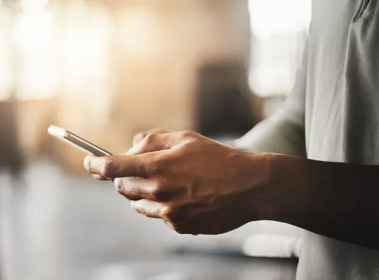 Hände halten und tippen auf einem weißen Smartphone. Die Person trägt ein helles Oberteil.