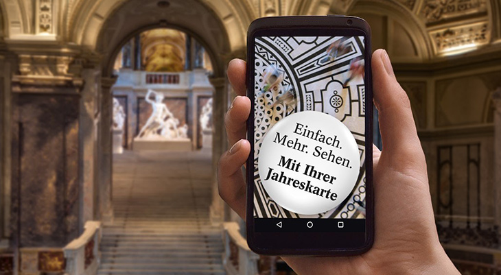 Smartphone zeigt Museum-App mit Text "Einfach. Mehr Sehen. Mit Ihrer Jahreskarte" in historischem Museumsgebäude