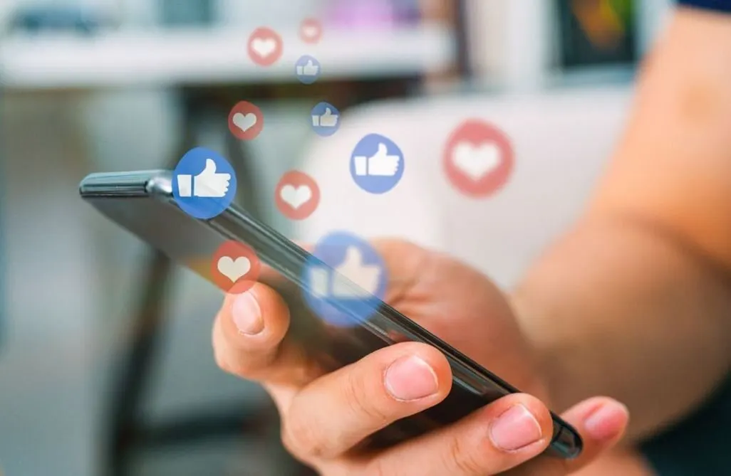 Person haelt ein Smartphone in der Hand mit digitalen Social Media Symbolen und Herz