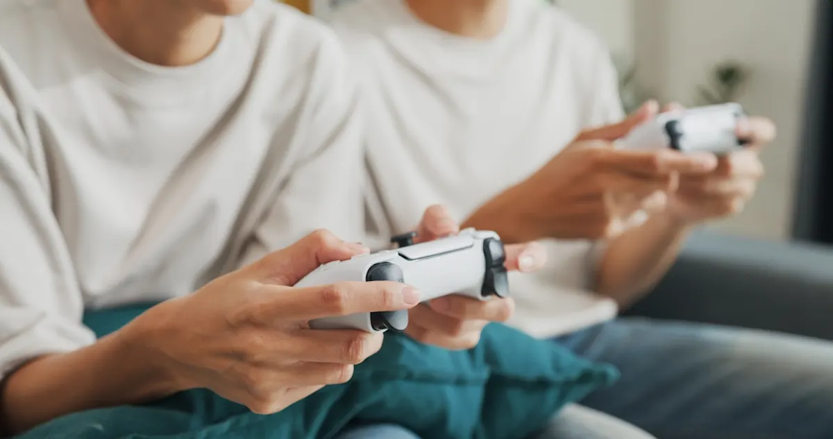 Nahaufnahme: Zwei Personen spielen mit weißen Gamecontrollern auf dem Sofa.