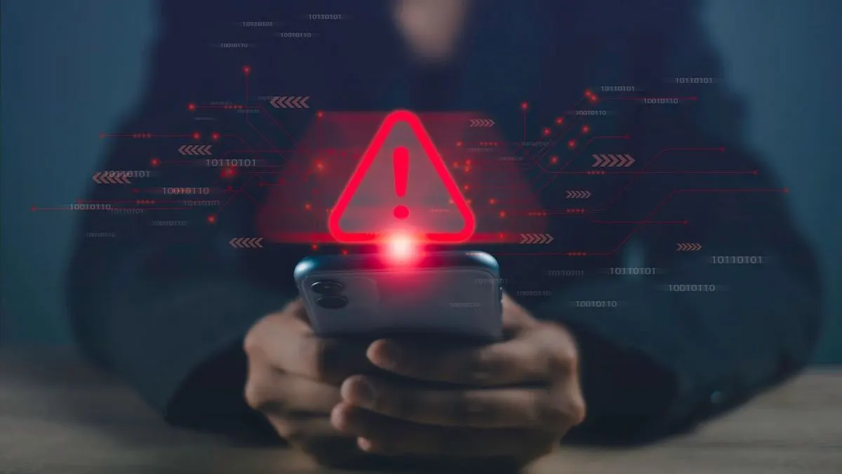 Eine Person hält ein Smartphone mit einem roten Warnsymbol und digitalen Grafiken.