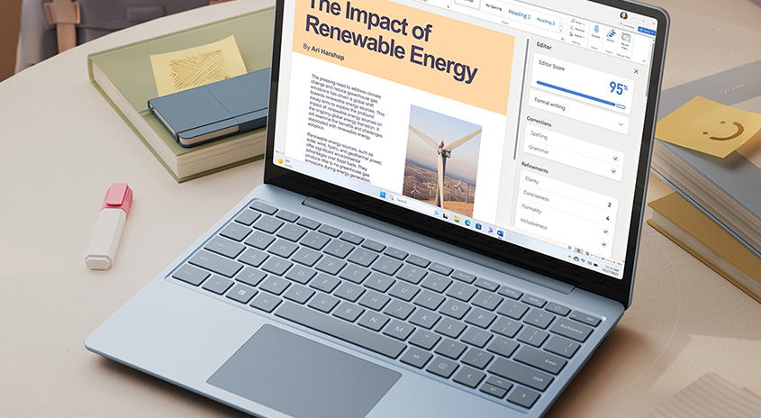 Ein Laptop zeigt einen Artikel über erneuerbare Energien. Daneben liegen Bücher und Notizen auf einem Tisch.