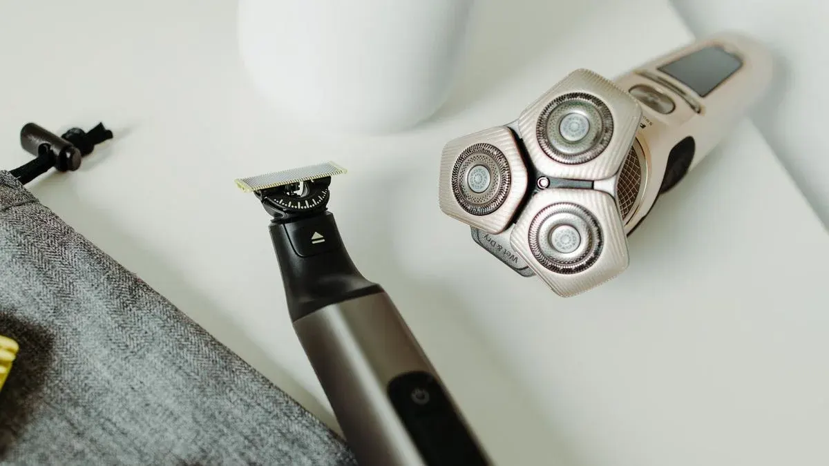 Grauer Stoffbeutel mit Kordel, ein schwarzer Trimmer mit silberner Klinge und ein heller Rasierer mit drei Rotationsköpfen und "Wet & Dry".