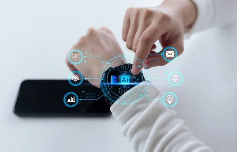 Mann tippt auf eine Smartwatch, die er am Arm trägt. Am Display ist das Wort "AI" zu lesen. Im Hintergrund liegt ein Smartphone.