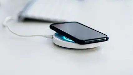 Smartphone liegt auf einer kabellosen Ladestation auf einem Schreibtisch.