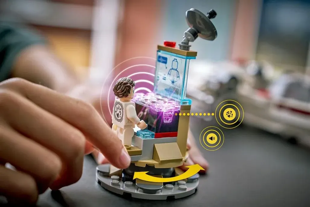 Hand dreht kleines LEGO Spielset mit Minifigur vor leuchtendem Hologramm-Display und Satellitenschüssel.
