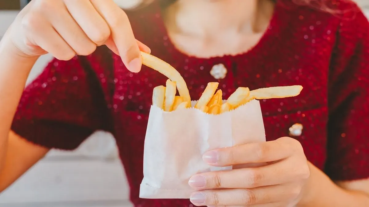 Eine Person nimmt ein Pommes Frites aus einer weißen Papiertüte mit weiteren Pommes.