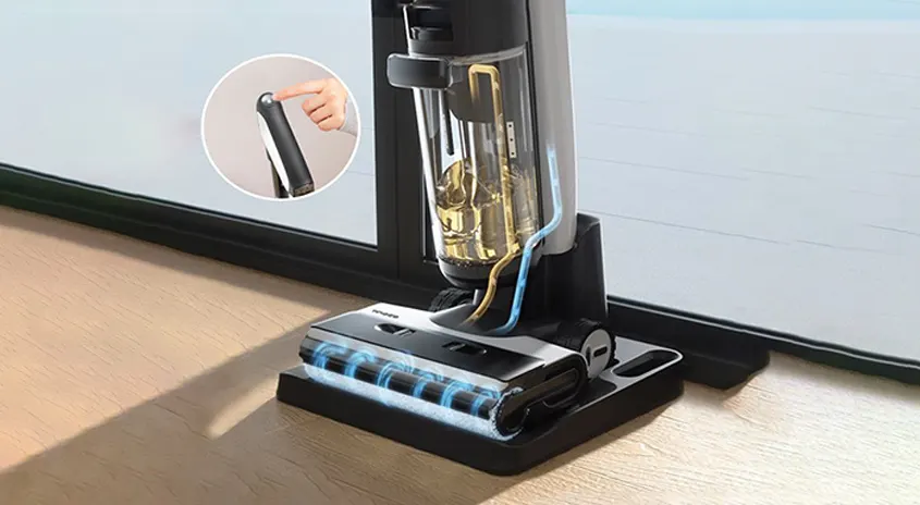 Ein schwarzer Staubsauger steht auf einem Holzboden vor einem Fenster. Der Staubsauger hat einen durchsichtigen Behälter mit goldfarbenem Inhalt.