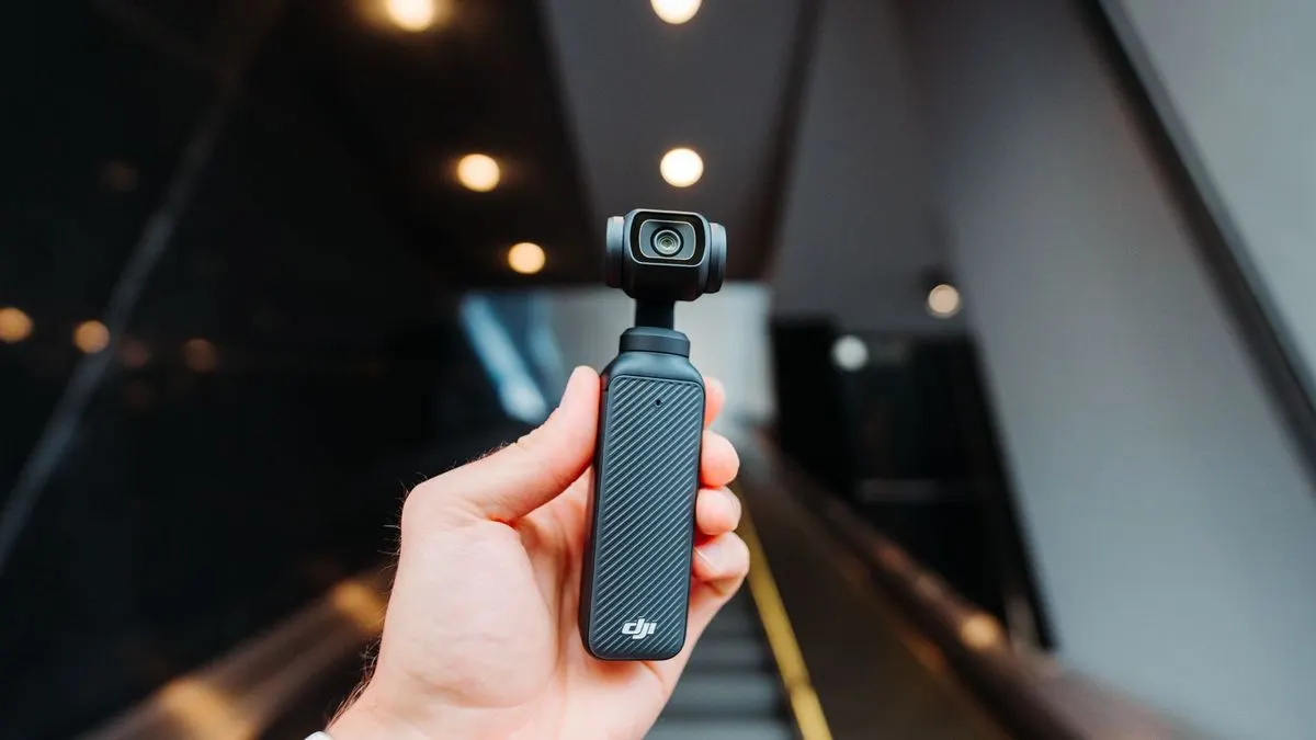 Hand haelt eine kleine schwarze DJI Kamera mit Gimbal, unscharfer Hintergrund mit Lichtern.