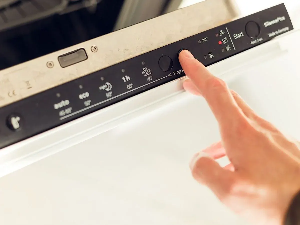 Hand drückt auf eine Taste in der Bedienleiste des Geschirrspülers